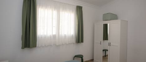 Une pièce comprenant un lit, une armoire, un petit tabouret et une fenêtre avec des rideaux.
