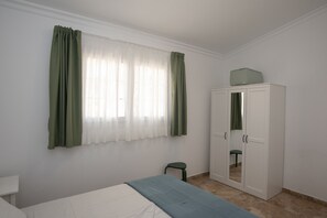 Een kamer met een bed, een kledingkast, een klein krukje en een raam met gordijnen.