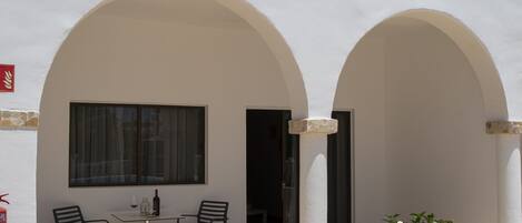 Un bâtiment blanc avec deux arcades et une fenêtre. On y voit deux chaises et une table à l’extérieur.
