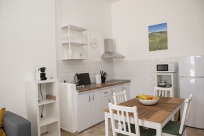 A compact kitchen with white cabinets, a microwave, a sink, and a dining area with a table and chairs.