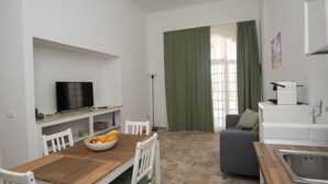 Un ambiente compatto con angolo ristoro, televisore, divano e angolo cottura.