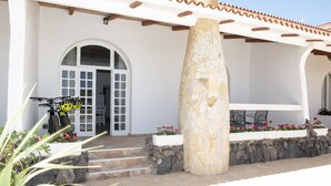 Un edificio bianco con una colonna in pietra, un portico con sedie e una bicicletta parcheggiata davanti.