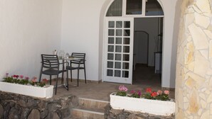 A covered patio with a table and chairs, a stone wall, and a door leading to an interior space. - Apartment Aulaga on Finca Falcon Cresta (Agüimes)