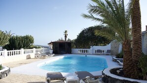 A swimming pool with lounge chairs, a covered seating area, and a palm tree. - Apartment Aulaga on Finca Falcon Cresta (Agüimes)