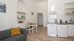 A compact kitchen with white appliances, a dining area with a table and chairs, and a sofa with a mustard-colored cushion. - Apartment Aulaga on Finca Falcon Cresta (Agüimes)