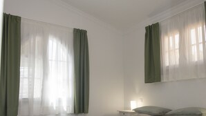 A bedroom with a bed, a nightstand, a wall-mounted light, and a window with curtains. - Apartment Aulaga on Finca Falcon Cresta (Agüimes)