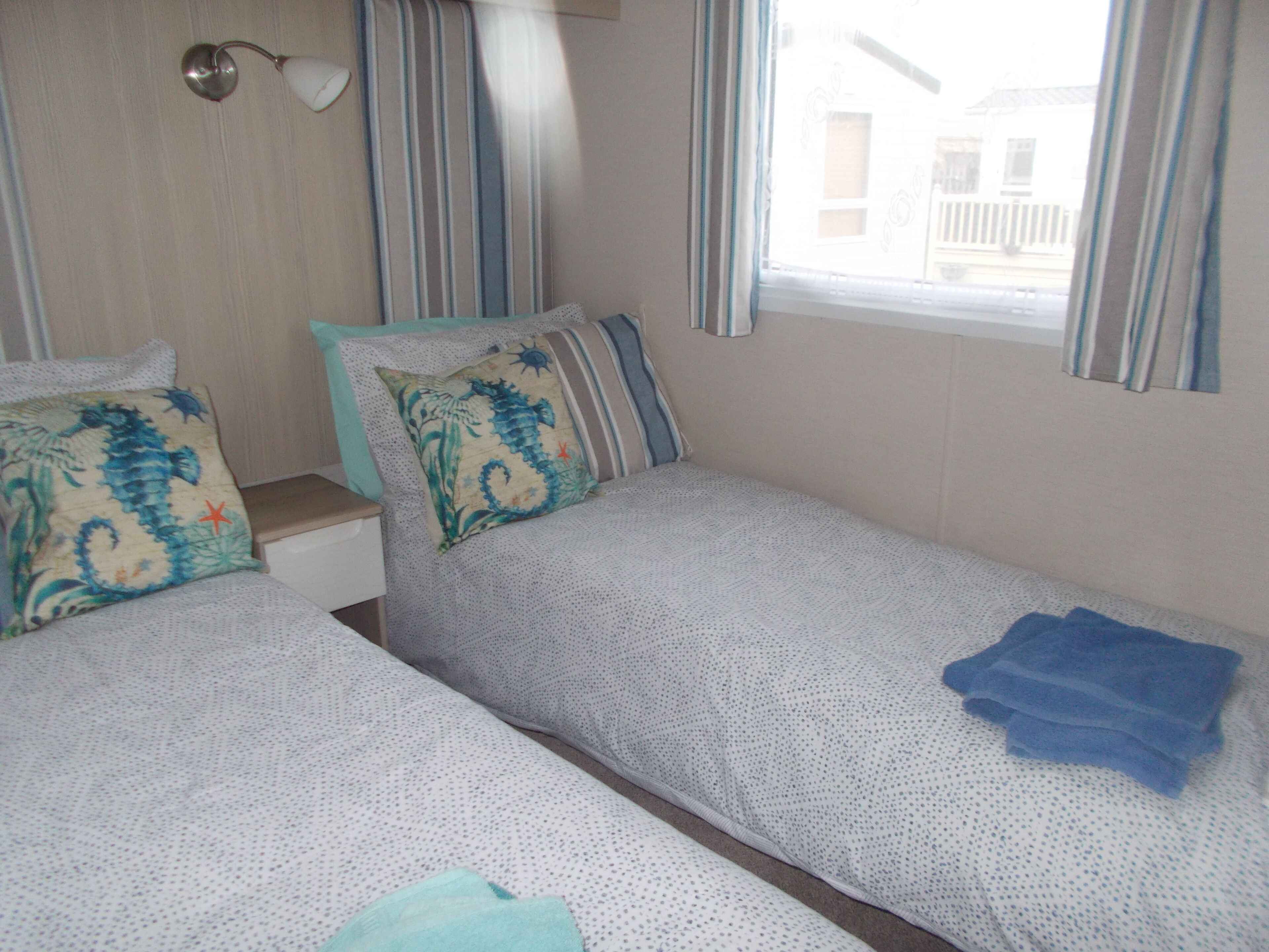 A room with two single beds, striped curtains, and a window with a view of a building outside.