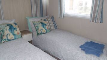 Une chambre avec deux lits simples, des rideaux à rayures et une fenêtre donnant sur un bâtiment à l’extérieur.