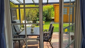 Un invernadero con puerta de cristal, una mesa de patio con sillas y una valla de madera al fondo.