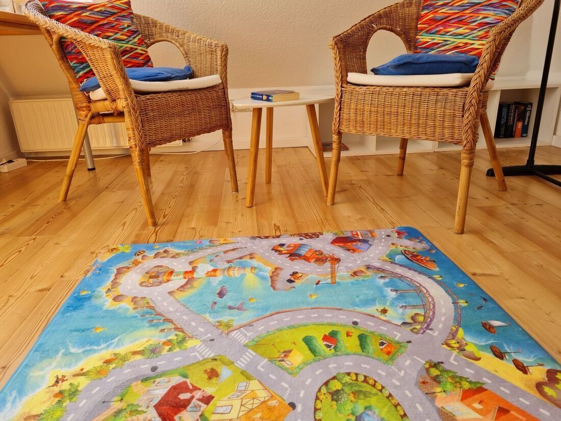 Two wicker chairs with blue cushions, a small white table, and a colorful play mat with a road and vehicles.