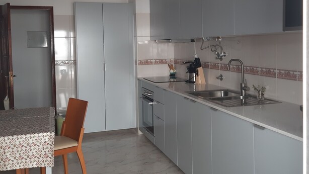 Una cucina moderna con mobili grigi, un lavello in acciaio inossidabile e un'area pranzo con tavolo e sedie.