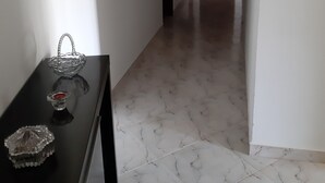 Un corridoio con pavimento in marmo, un tavolo nero con oggetti decorativi e quadri appesi alle pareti.