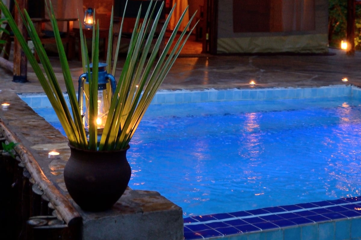 Un espace aménagé au bord de la piscine, comprenant une structure en forme de tente, un pot de fleurs et une lanterne.