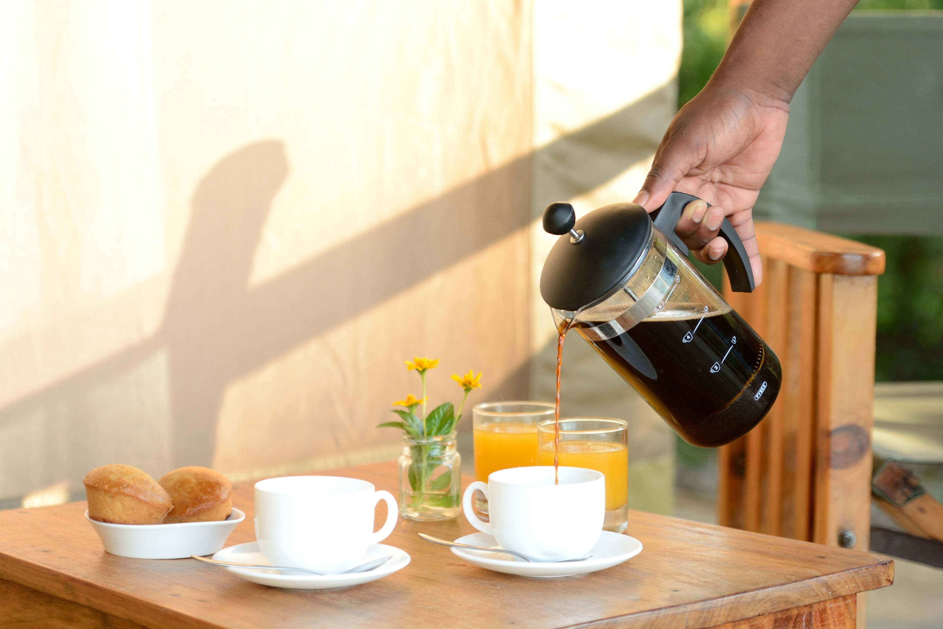 Ein Frühstücksangebot mit einer Kaffeemaschine, die in eine Tasse läuft, zwei Muffins in einer kleinen Schale und ein Glas Orangensaft auf einem Holztisch.
