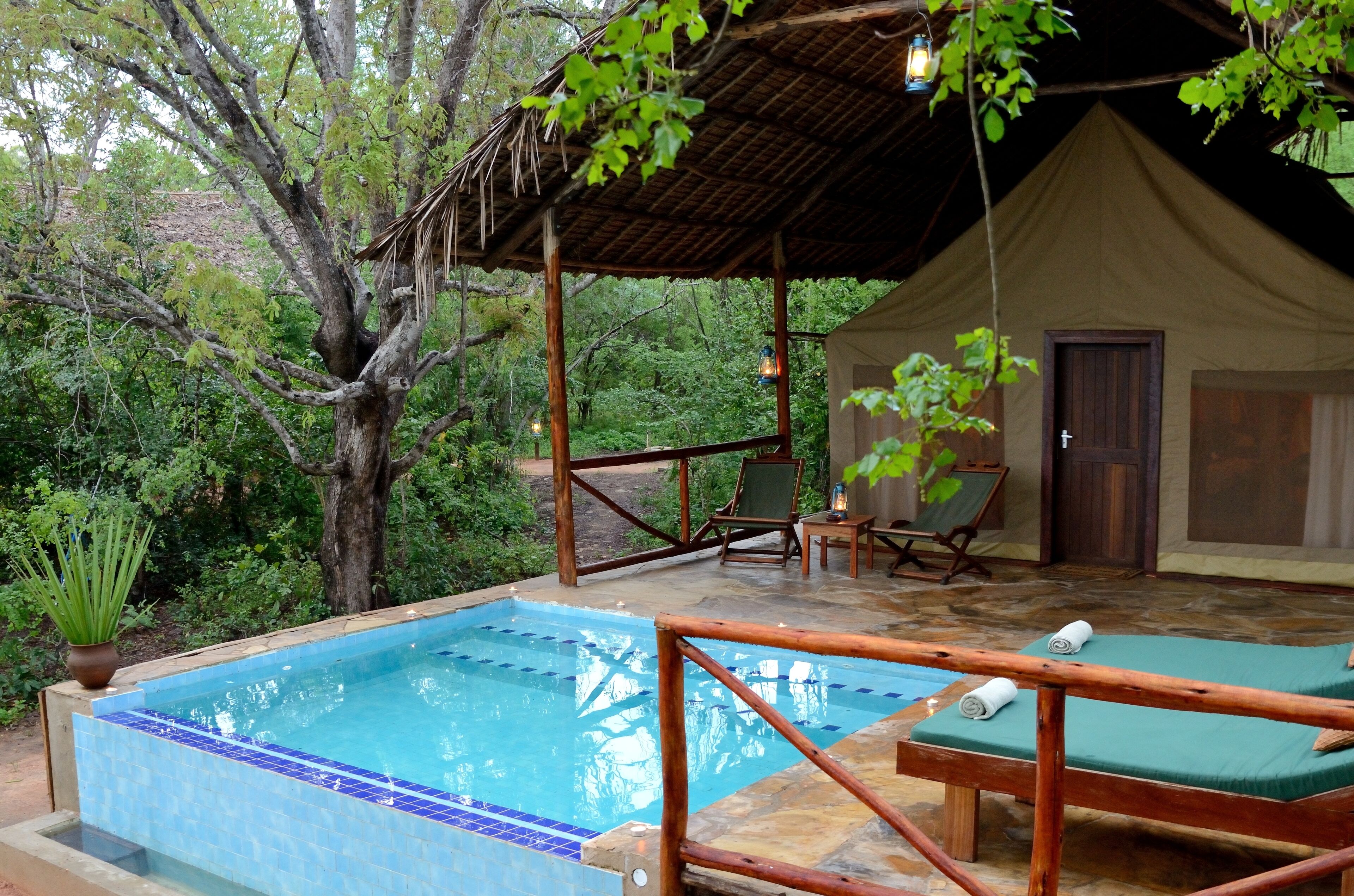 A pool area with a wooden deck, lounge chairs, and a tented structure.