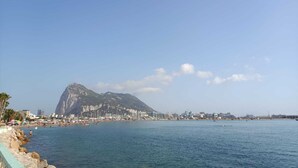 A coastal cityscape with a prominent mountain in the background, a beach with people and umbrellas, and a marina with boats.