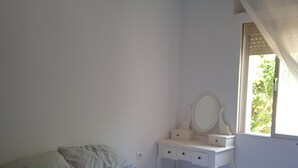 A bedroom with a bed, a nightstand, a dresser, a mirror, and a window with curtains.