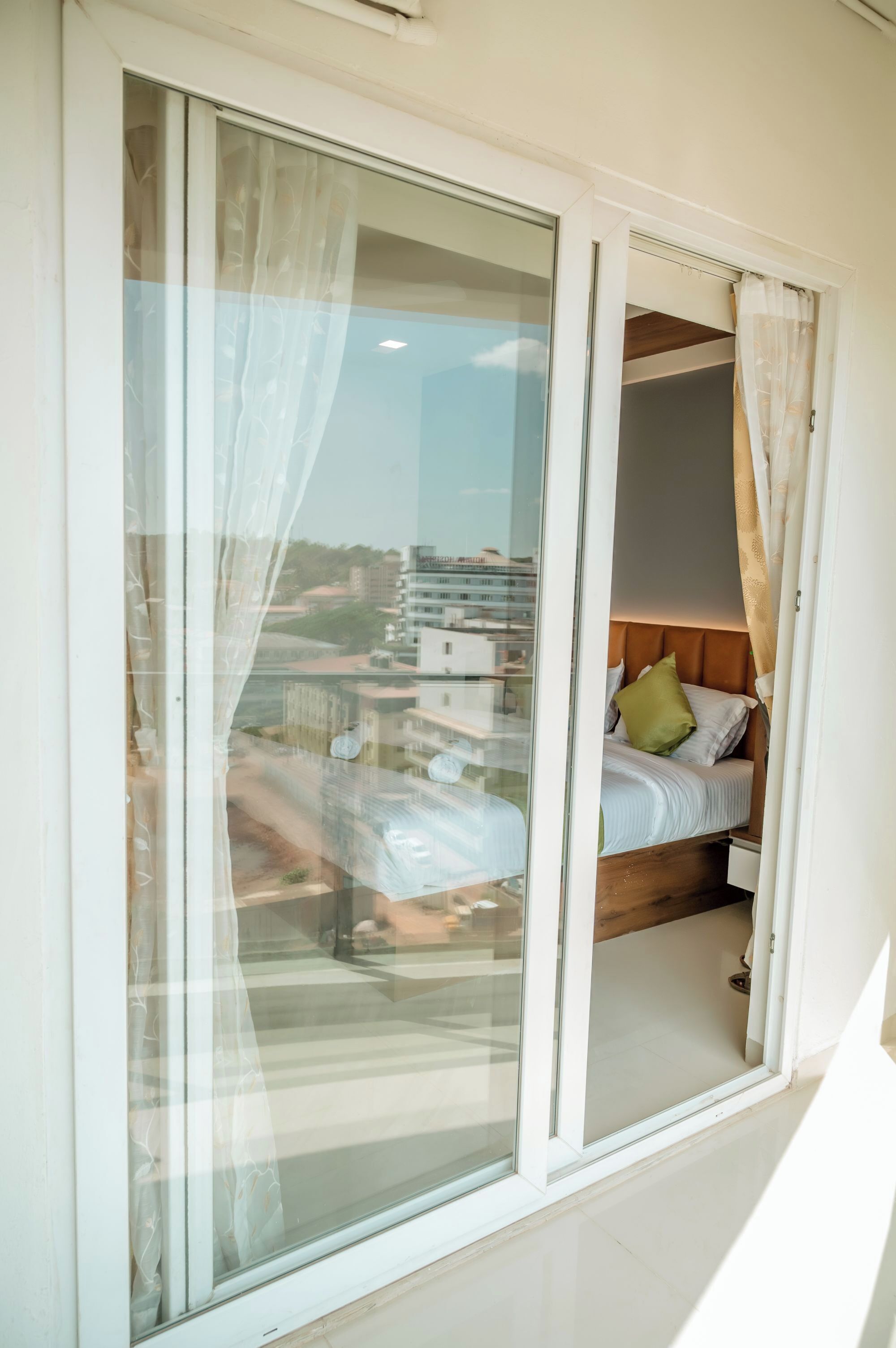 A bedroom with a bed, a window with curtains, and a view of buildings outside.