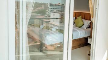 A bedroom with a bed, a window with curtains, and a view of buildings outside.