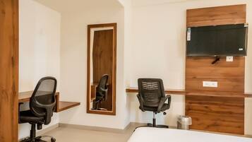 Ein Hotelzimmer mit einem Bett, zwei Bürostühlen, einem Holztisch, einem Spiegel und einem an der Wand befestigten Fernseher.