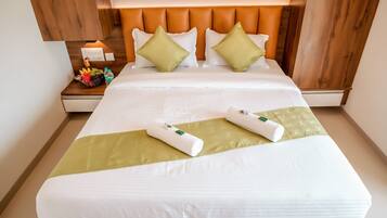 Una cama bien hecha con sábanas blancas, dos almohadas verdes y dos toallas enrolladas.