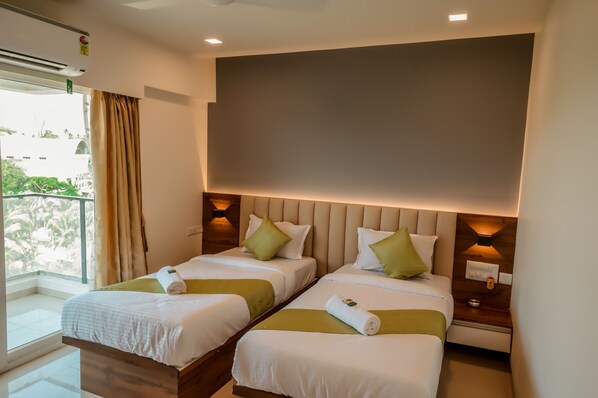 Habitación de hotel con dos camas, paredes color beige y vistas al exterior con vegetación.