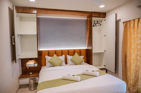 Habitación de hotel con cama, mesita de noche, espejo, armario y cortina de ducha.