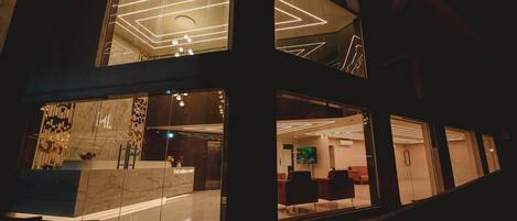 A modern hotel lobby with a reception desk, seating area, and a large TV screen.