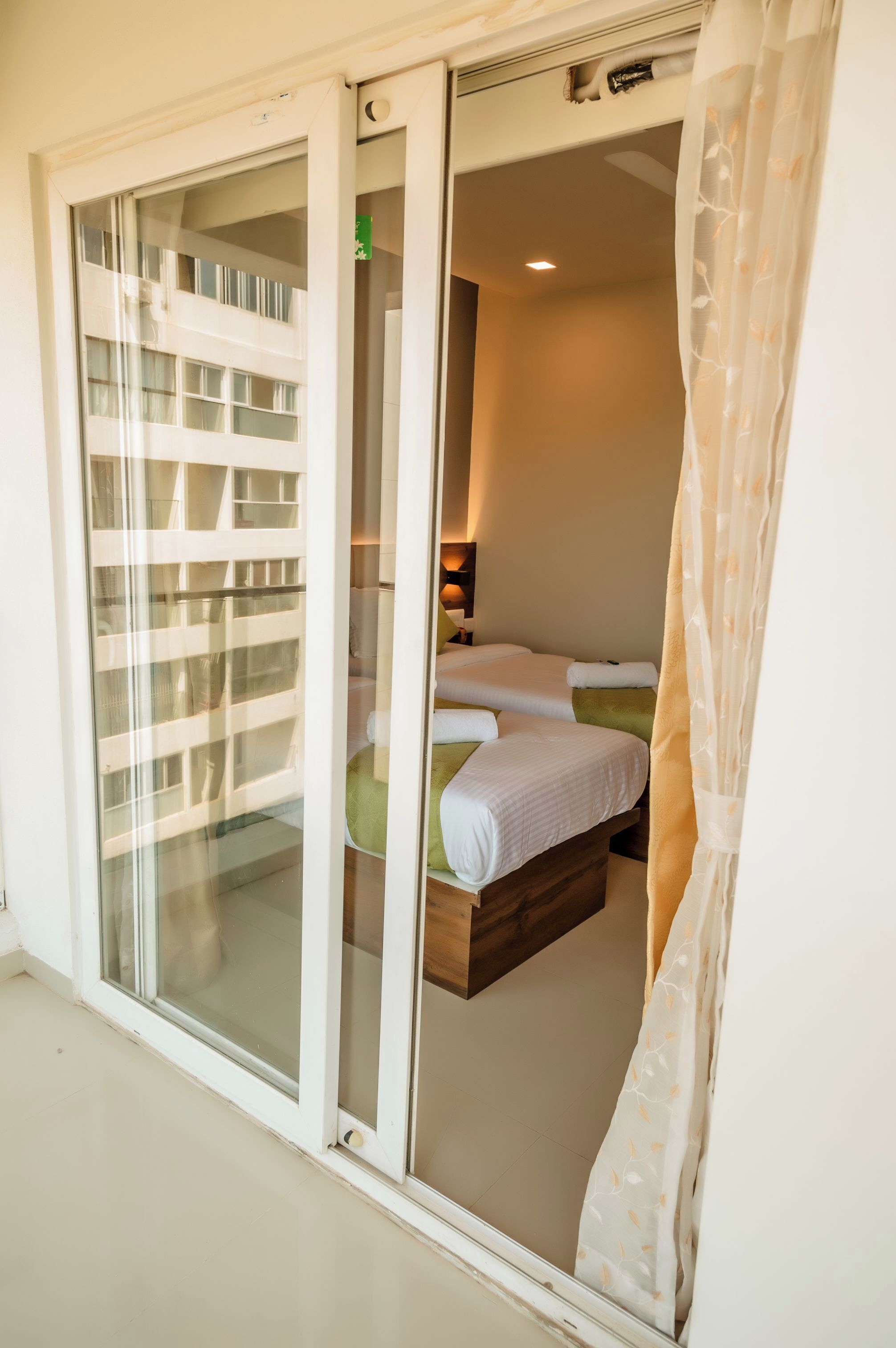 Une chambre d’hôtel dotée d’une porte-fenêtre coulissante donnant sur un balcon, d’un lit avec une tête de lit en bois et d’une table de chevet avec une lampe.