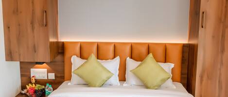 Habitación de hotel con una cama grande, cabecero de madera y una mesita de noche con una cesta de frutas y botellas.
