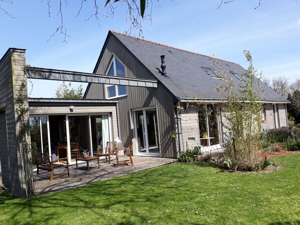 Une maison moderne dotée d’un grand patio, d’un espace salon extérieur abrité et d’une pelouse bien entretenue.