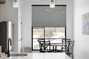 A modern kitchen with a large window, a dining area with chairs, and a refrigerator.