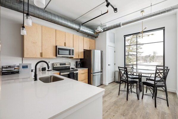 A modern kitchen with a large island, stainless steel appliances, and a dining area with a large window.