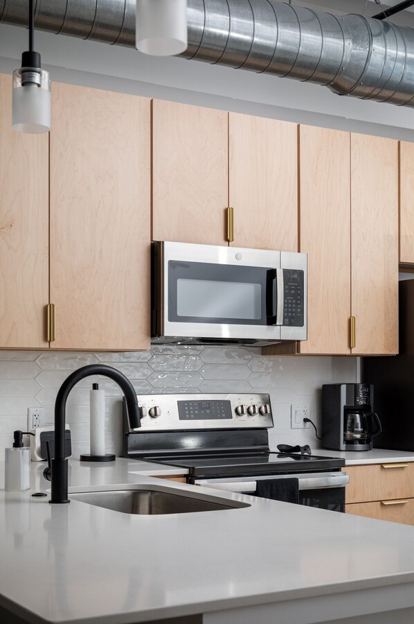 A modern kitchen with wooden cabinets, a stainless steel microwave, a gas stove, and a coffee maker. - Base of Old Mission Peninsula 2BR Condo w/ Rooftop Hot Tubs near East Bay Beach (Traverse City)