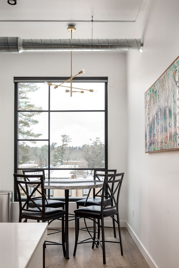 Un comedor con un ventanal grande, una lámpara moderna tipo candelabro y una obra de arte abstracta en la pared.