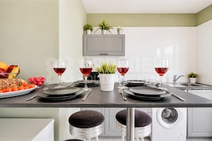 A modern kitchen with a dining table set for four, a washing machine, and a TV mounted above the counter.