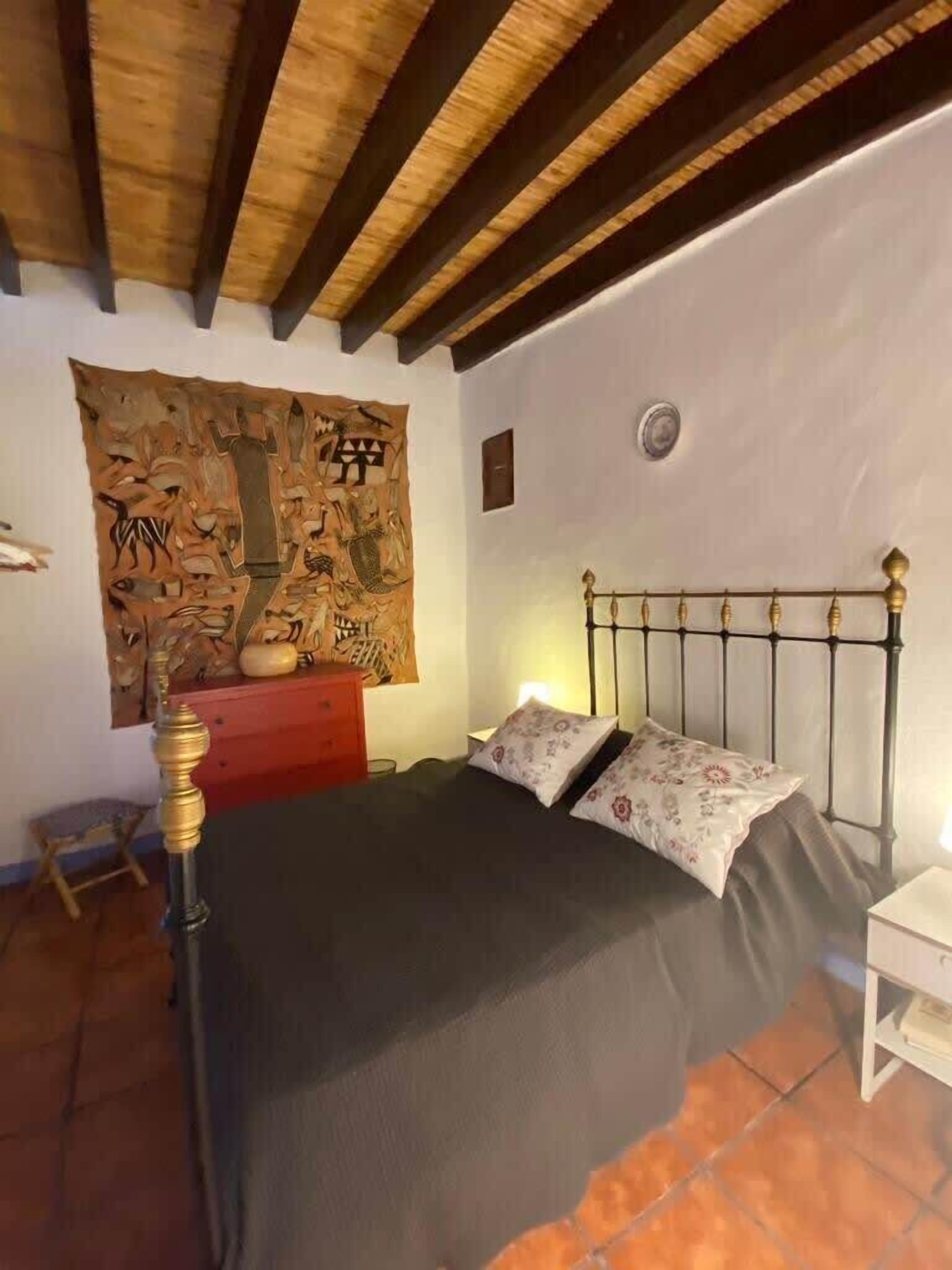 Een slaapkamer met een bed, een nachtkastje, een rode dressoir en een wandtapijt.