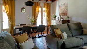 Ein Wohnzimmer mit einer Couch, einem Esstisch mit Stühlen und einer Decke mit freiliegenden Holzbalken.