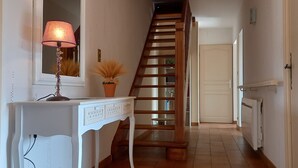 Eine Treppe mit hölzernem Geländer führt zu einer Tür. Eine weiße Konsole mit Lampe und Topfpflanze steht links davon.