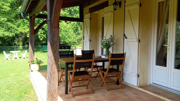 Ein überdachter Patio-Bereich mit Holztisch und -stühlen, einem Grill und einem Blumentopf.