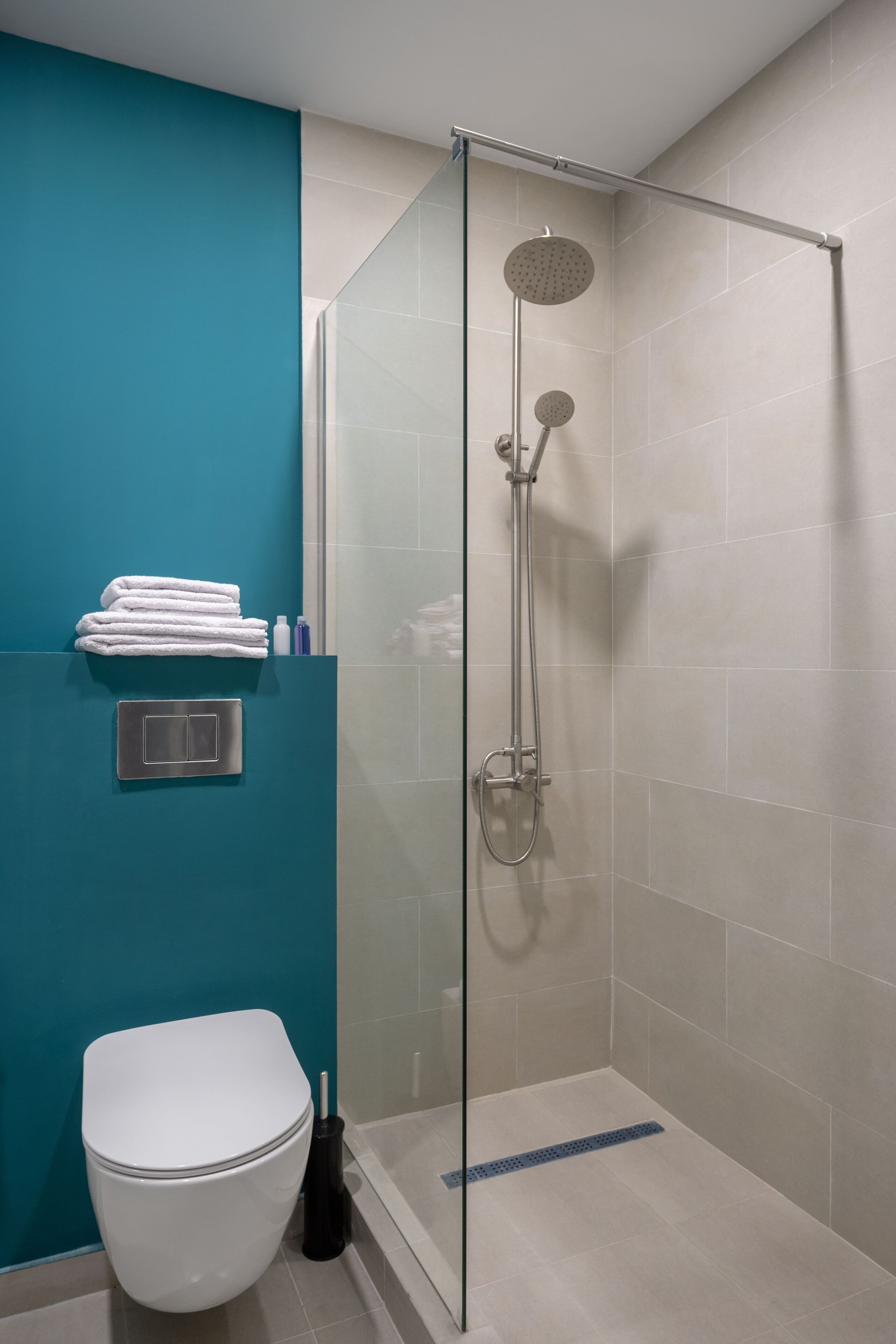 Un baño moderno con ducha acristalada, inodoro blanco y pared de acento color aguamarina.