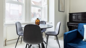 A dining area with a round table, four chairs, a vase, and a piano. - Modern Apartment in Walthamstow (London)