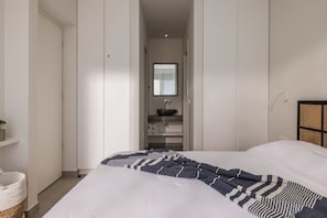 Een slaapkamer met een bed, een kast, een spiegel en een plank met handdoeken.
