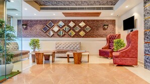 Eine moderne Lobby mit Marmorboden, einer gesteppten Couch, einem rot samtenen Sessel und einer Wand, die mit diamantförmigen Spiegeln verziert ist.