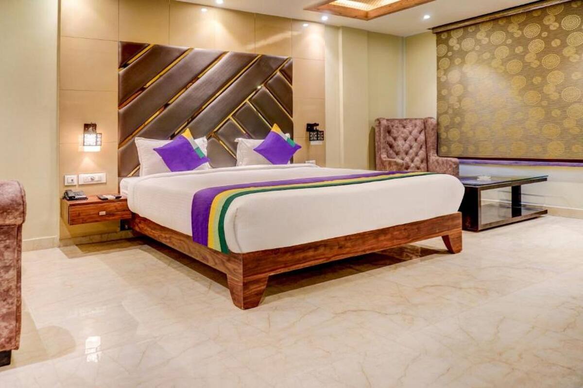 Ein modernes Hotelzimmer mit einem großen Bett, einem Holzkopfende, einem Nachttisch, einer Sitzecke mit einem Sessel und einem kleinen Tisch.