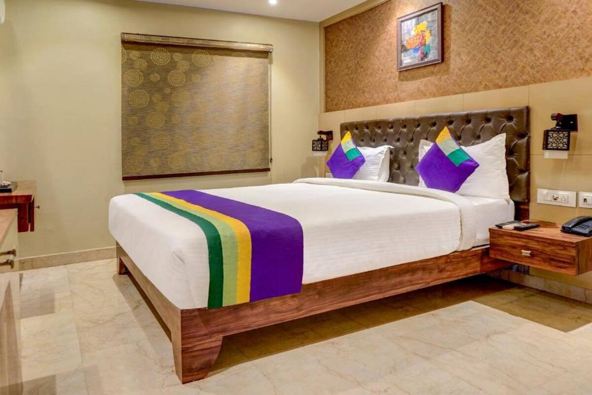 Ein Hotelzimmer mit einem großen Bett, einem Nachttisch aus Holz, einem Telefon und einer Wandleuchte.