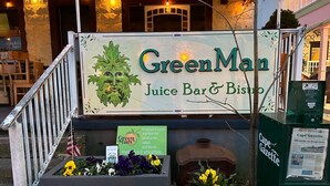 Un escaparate con un letrero que dice "Green Man Juice Bar & Bistro" y una exhibición de flores.