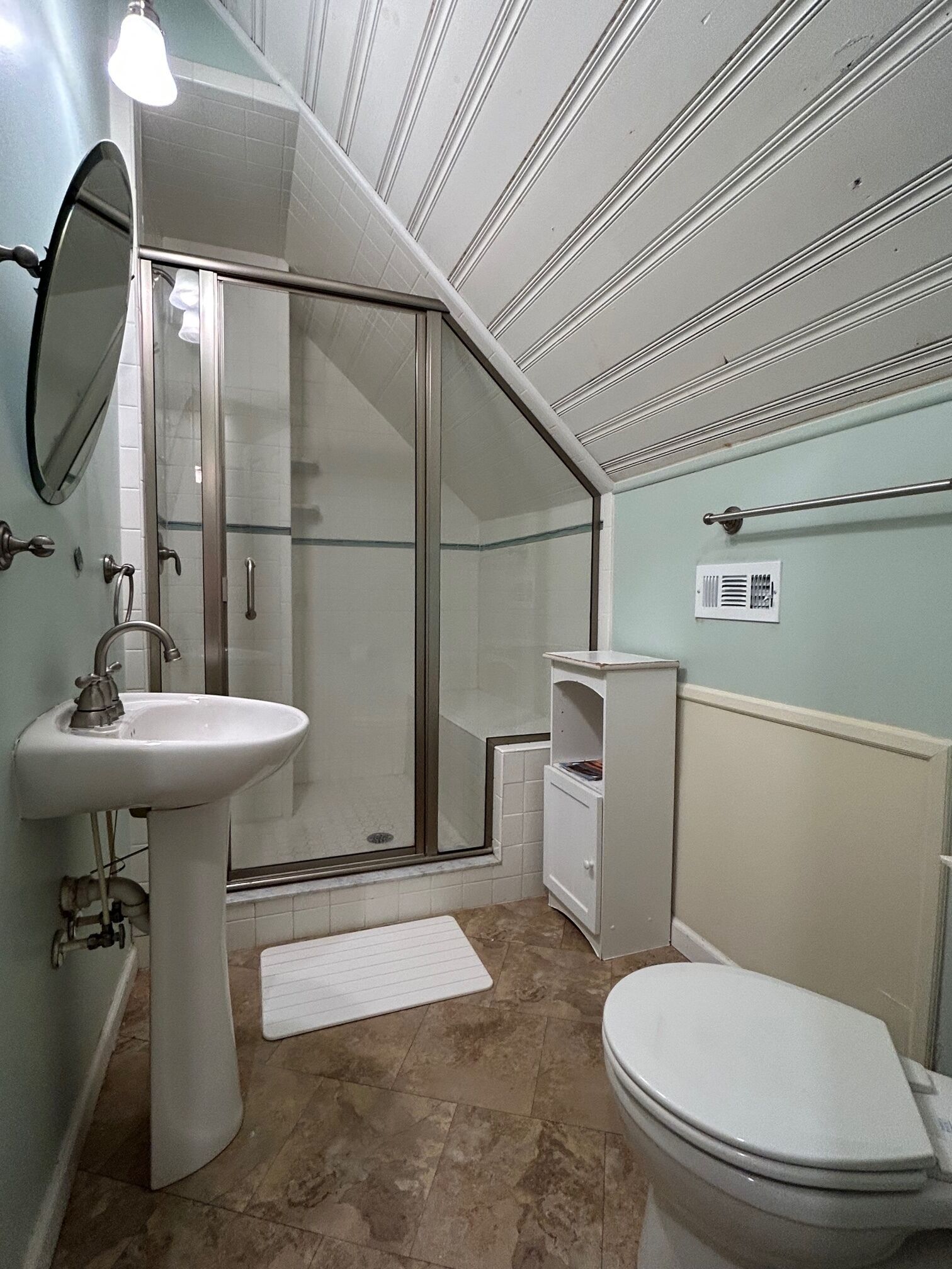 Een badkamer met douche, wastafel, toilet en een klein kastje.