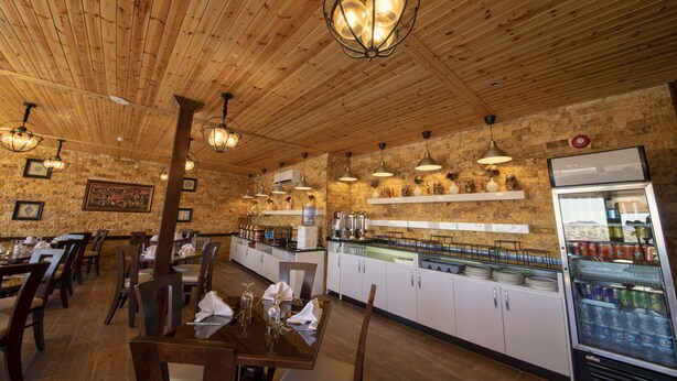 Ein Restaurant mit Holzbalkendecke und -wänden, Pendelleuchten, einer Buffettheke und einem mit Getränken gefüllten Kühlschrank.