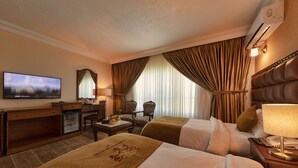 Ein Hotelzimmer mit zwei Betten, einem Fernseher, einem Schreibtisch mit Computer, einem Stuhl und einem kleinen Tisch mit Lampe.